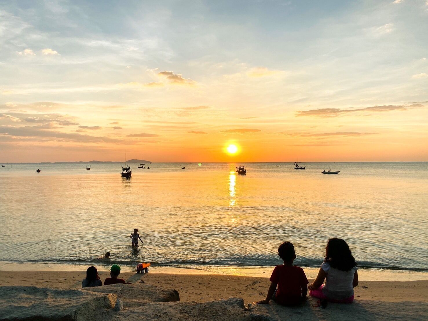 A beach scene with a sunset, calm sea, and boats.