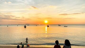 A beach scene with a sunset, calm sea, and boats.