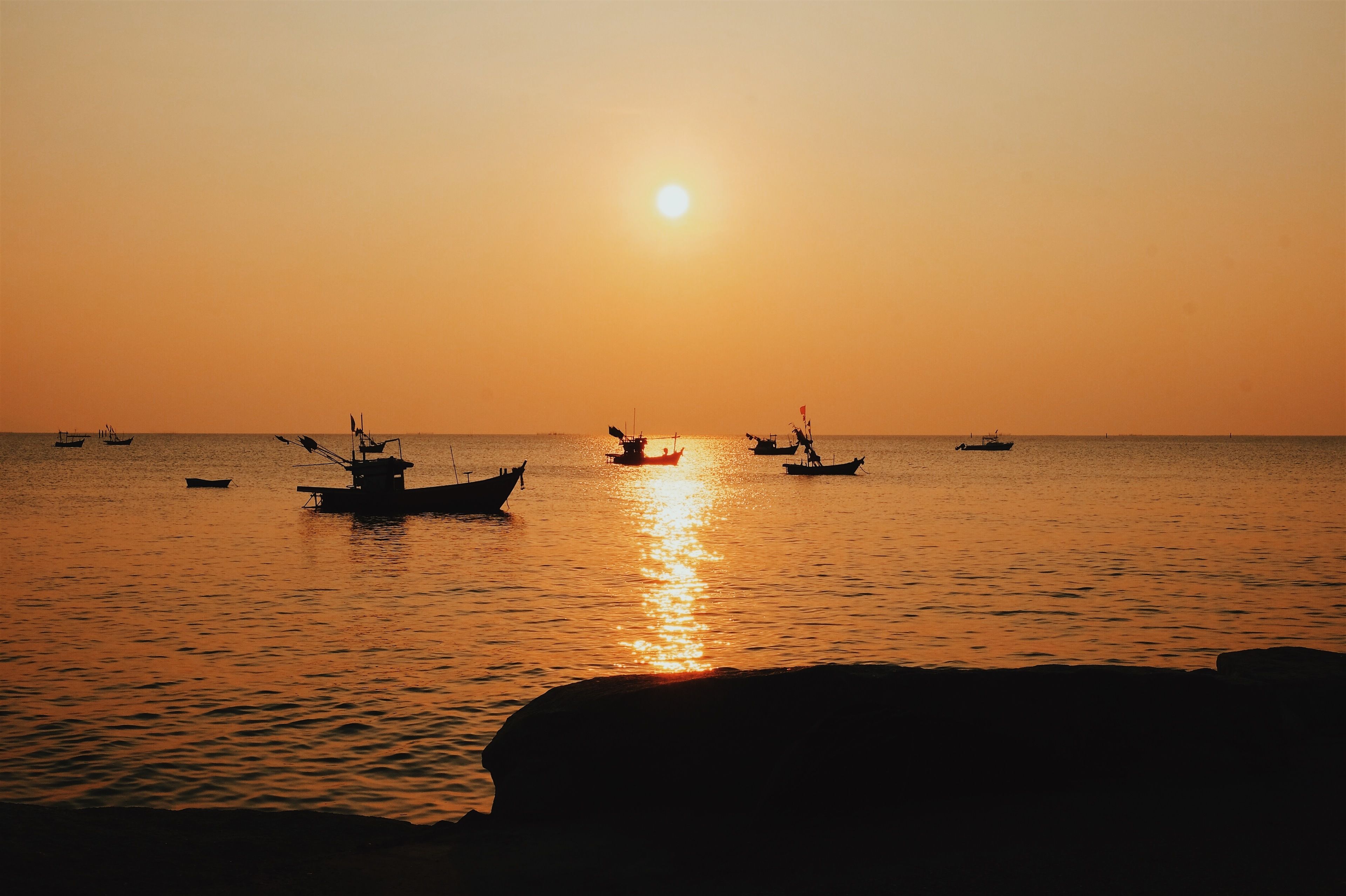 A sunset over a calm sea with several boats.