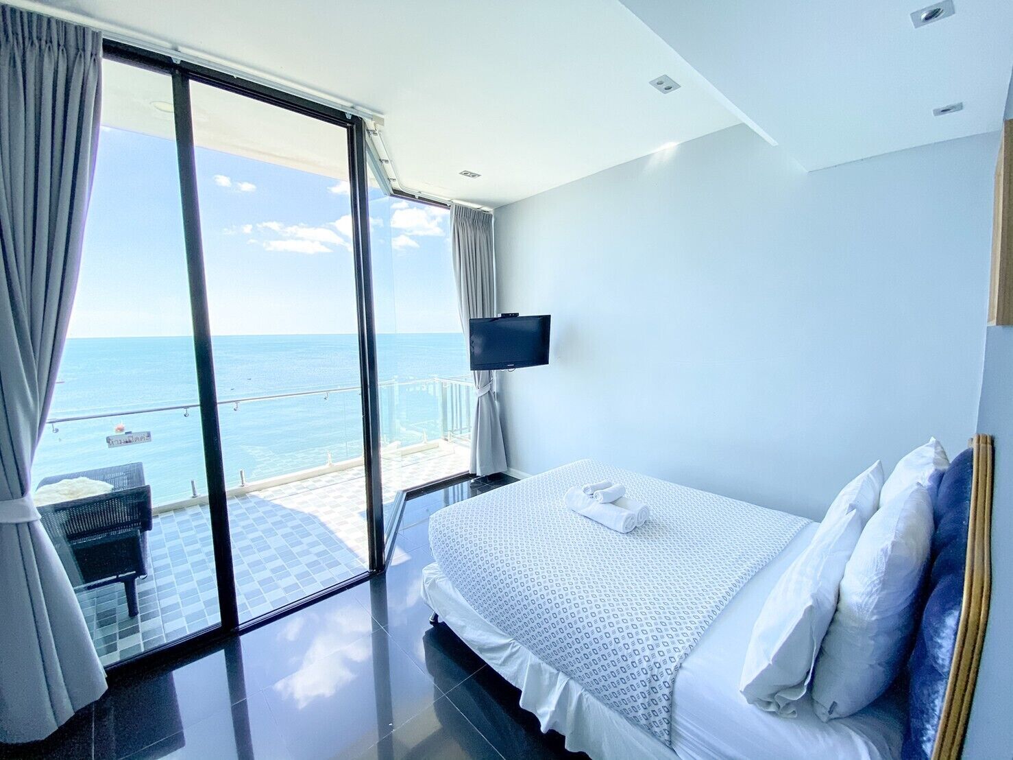A hotel room with a bed, a TV, and a view of the sea.