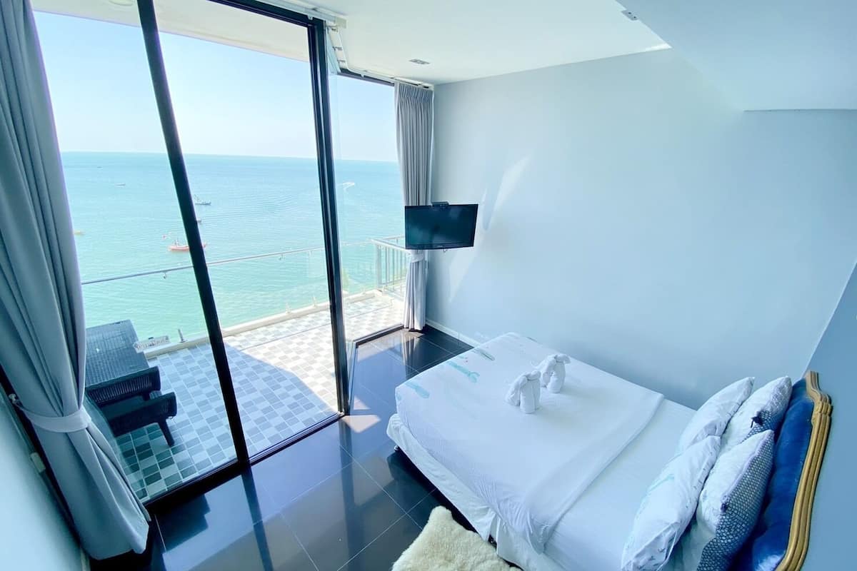 Ett modernt hotellrum med en stor säng, en TV och en balkong med utsikt över havet.