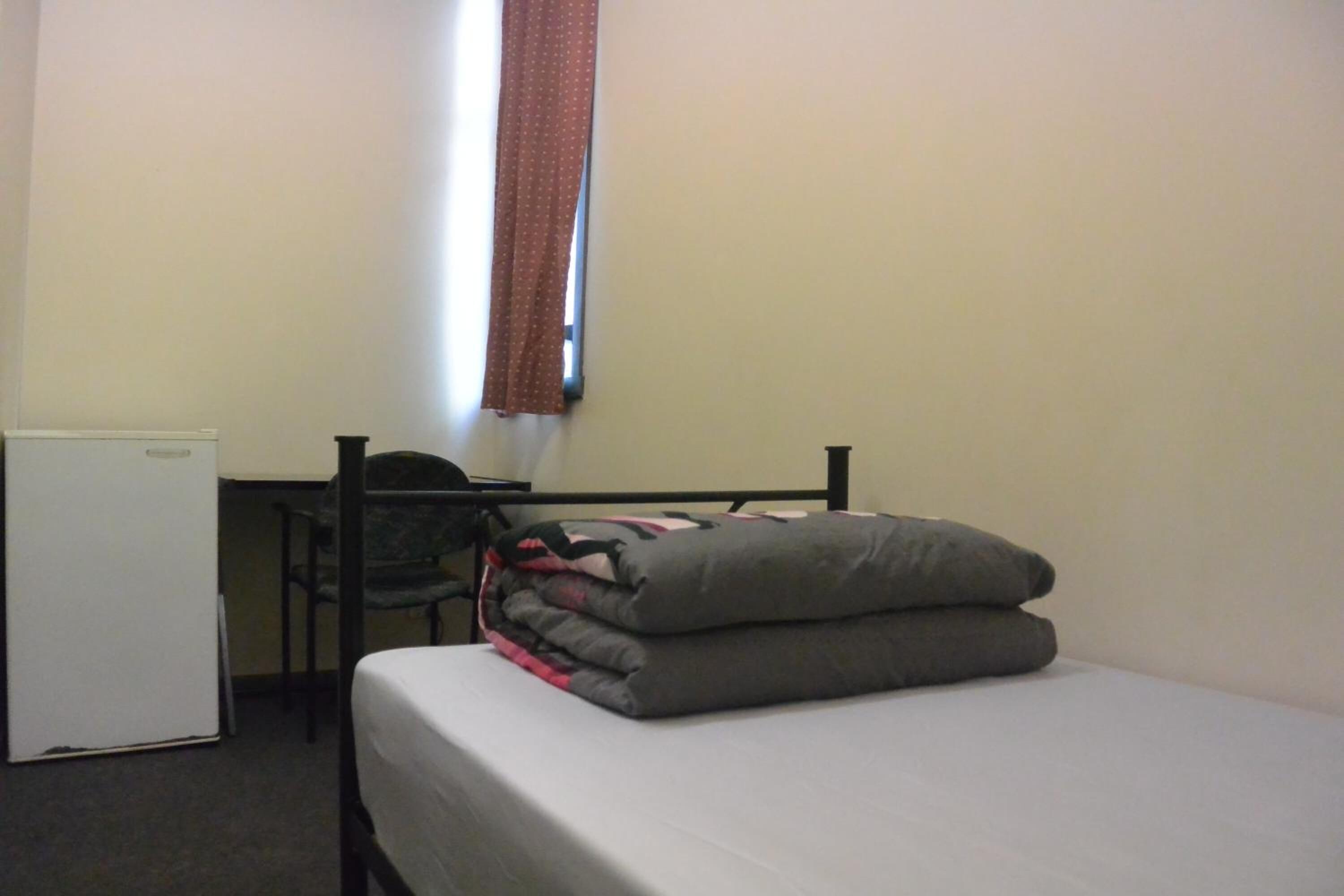 A small, simple room with a bed, a desk, and a chair.