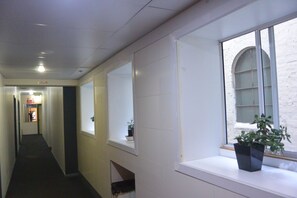 A hallway with a potted plant on a window sill, a door with a sign, and a brick wall visible through the window. - Elizabeth Hostel (Melbourne)