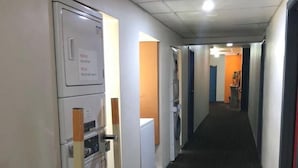 A hallway with a black carpet, white walls, and a row of appliances on the left.