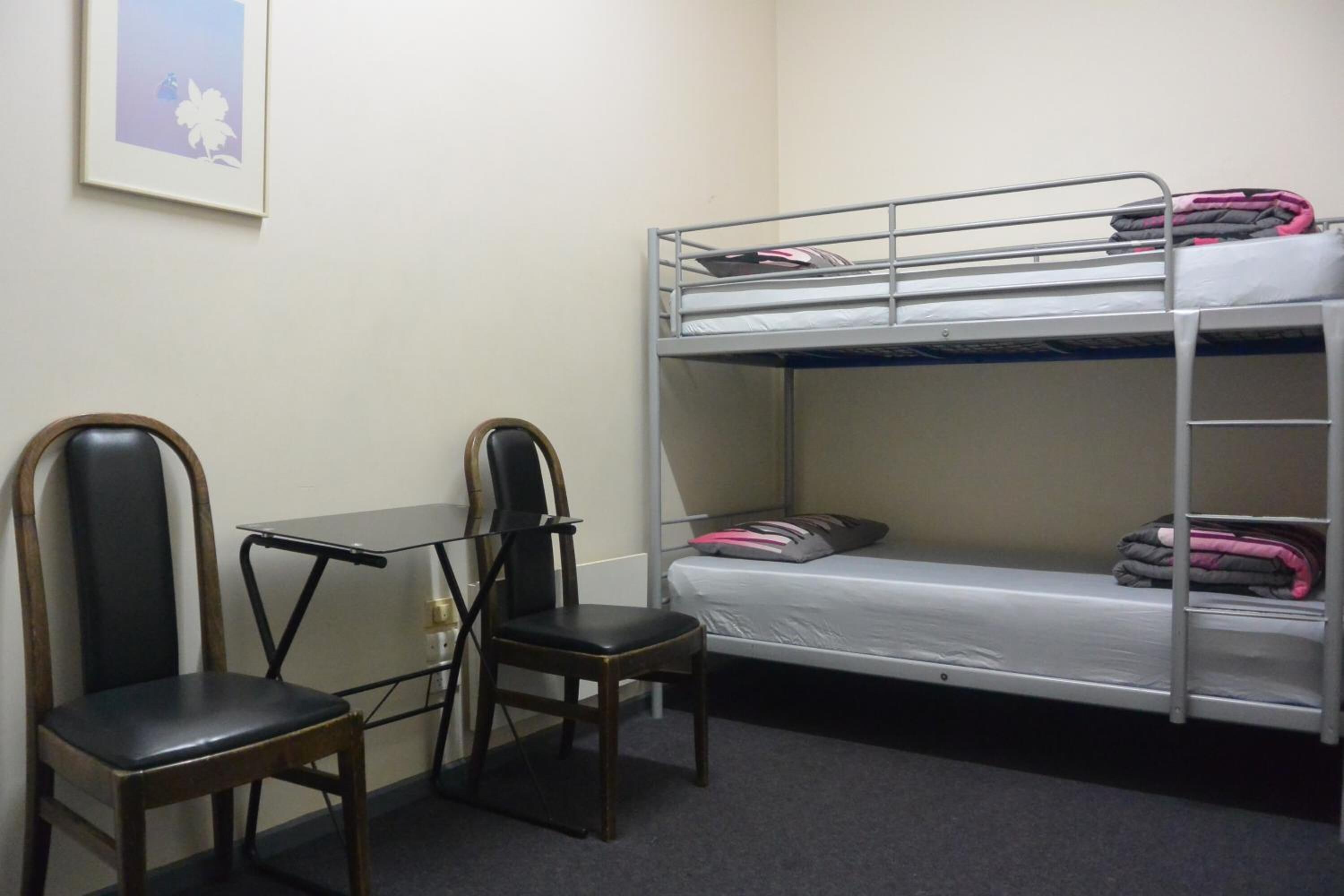A bunk bed with a desk and two chairs in a room with plain walls.