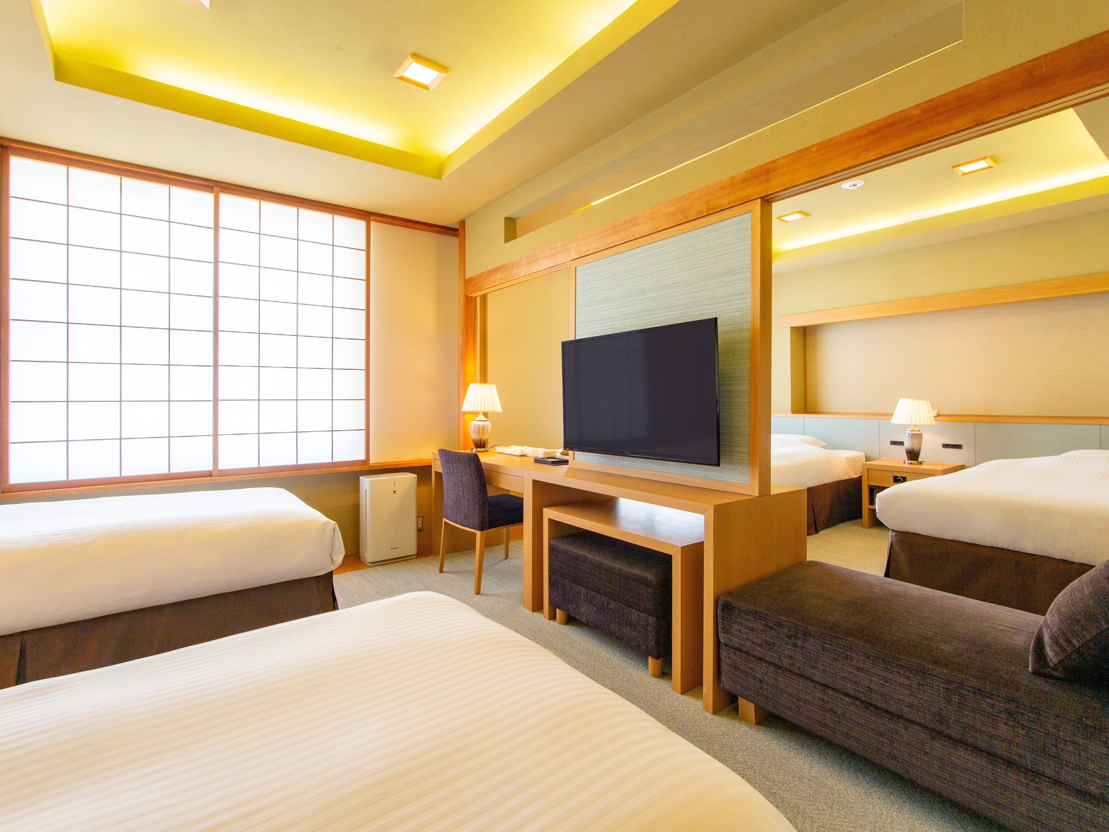A hotel room with two beds, a desk, a television, and a large window.