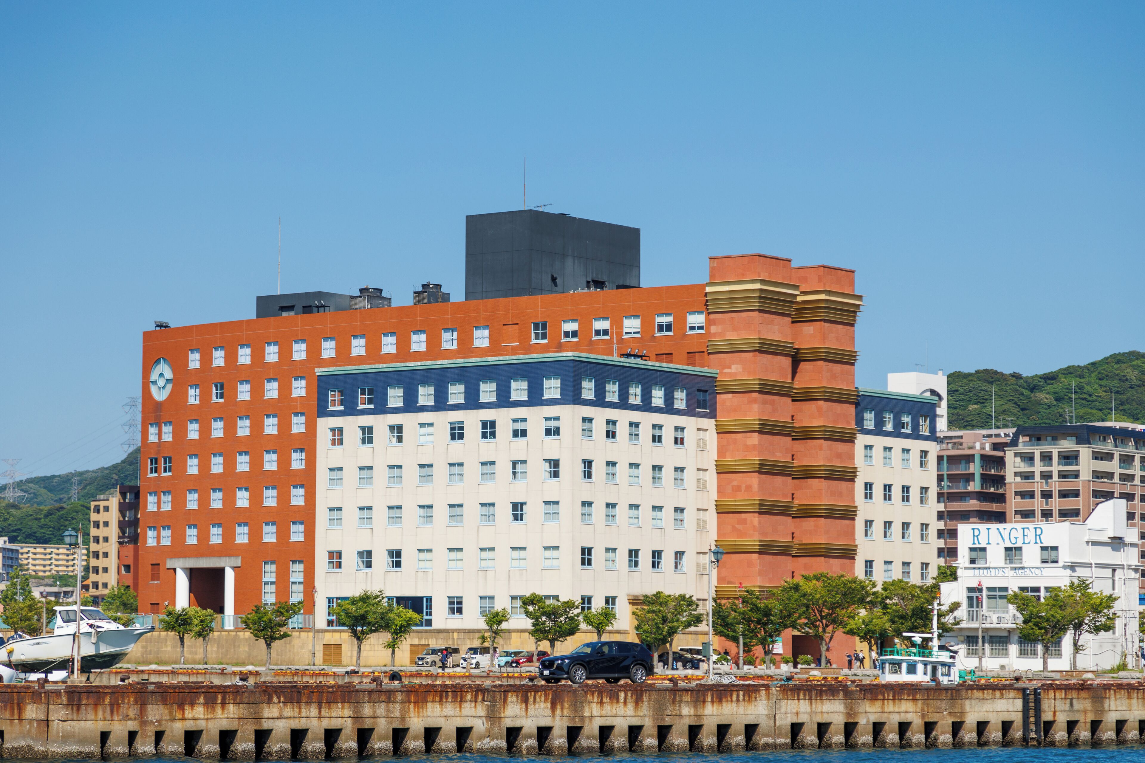 Un hotel de varios pisos con una destacada torre de reloj, un edificio central amplio y una estructura adyacente más pequeña.