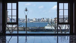 A room with a large window offering a view of a harbor with boats and a city skyline.