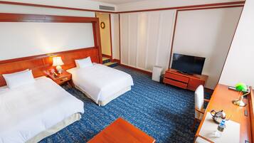 A hotel room with two beds, a desk with a television, a small table, and a wardrobe.