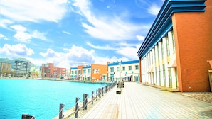 A waterfront promenade with buildings, a clear sky, and calm water.