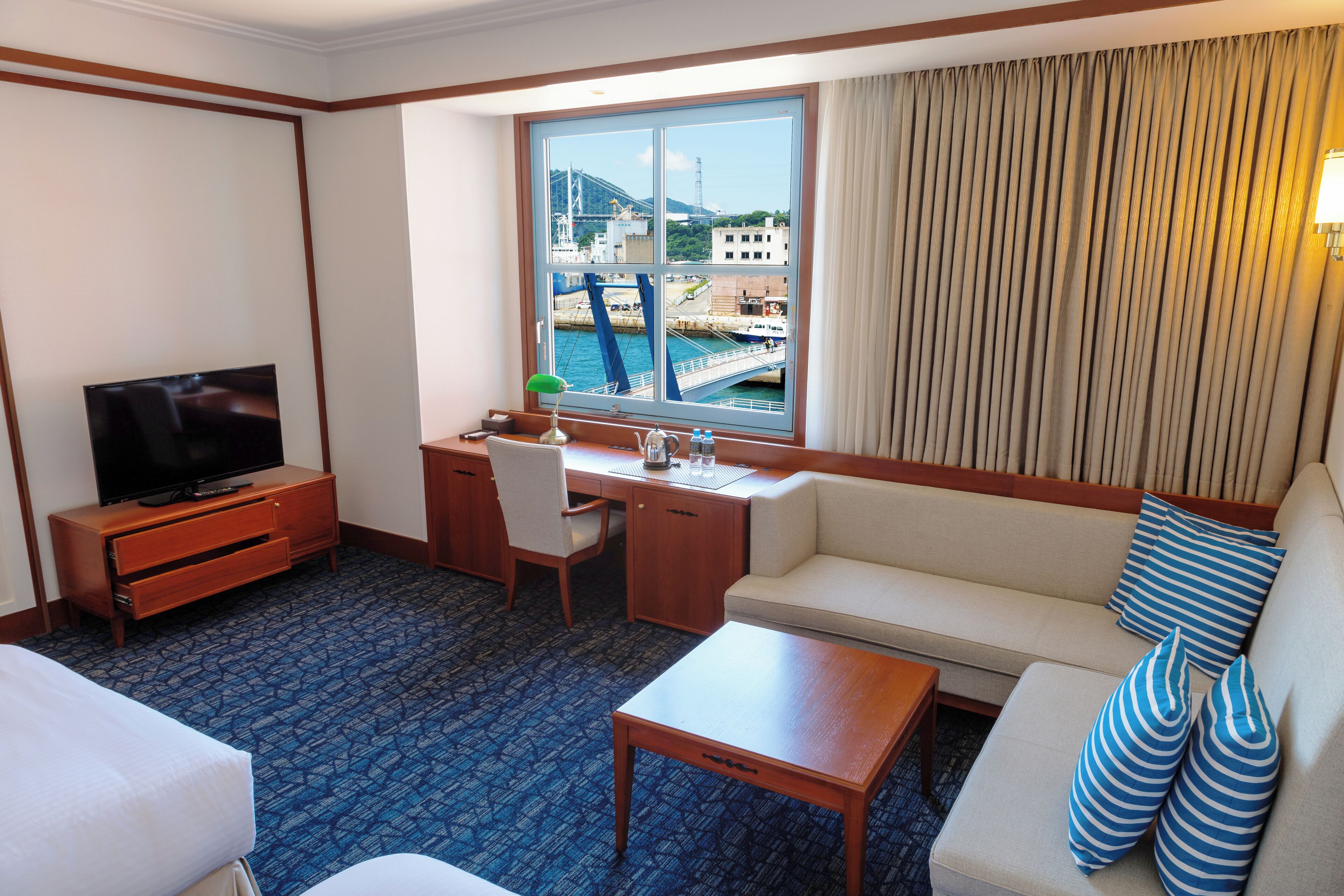 A hotel room with a TV, a desk, a sofa, and a view of a bridge and water.