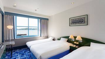 A hotel room with two beds, a desk, a chair, a window with curtains, a nightstand with lamps, and a framed picture on the wall.