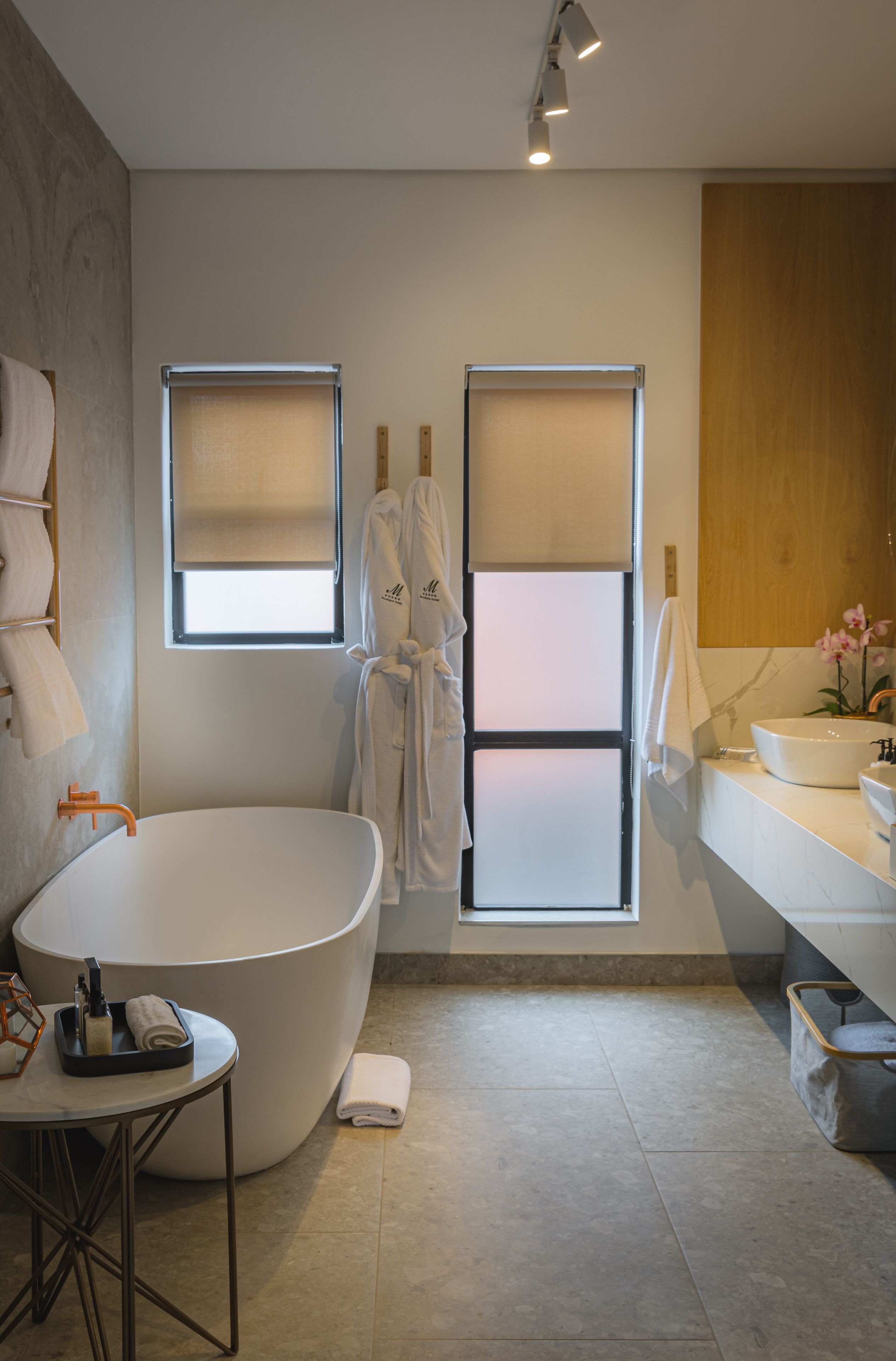 A modern bathroom with a freestanding bathtub, a vanity with a sink, and two windows with blinds.