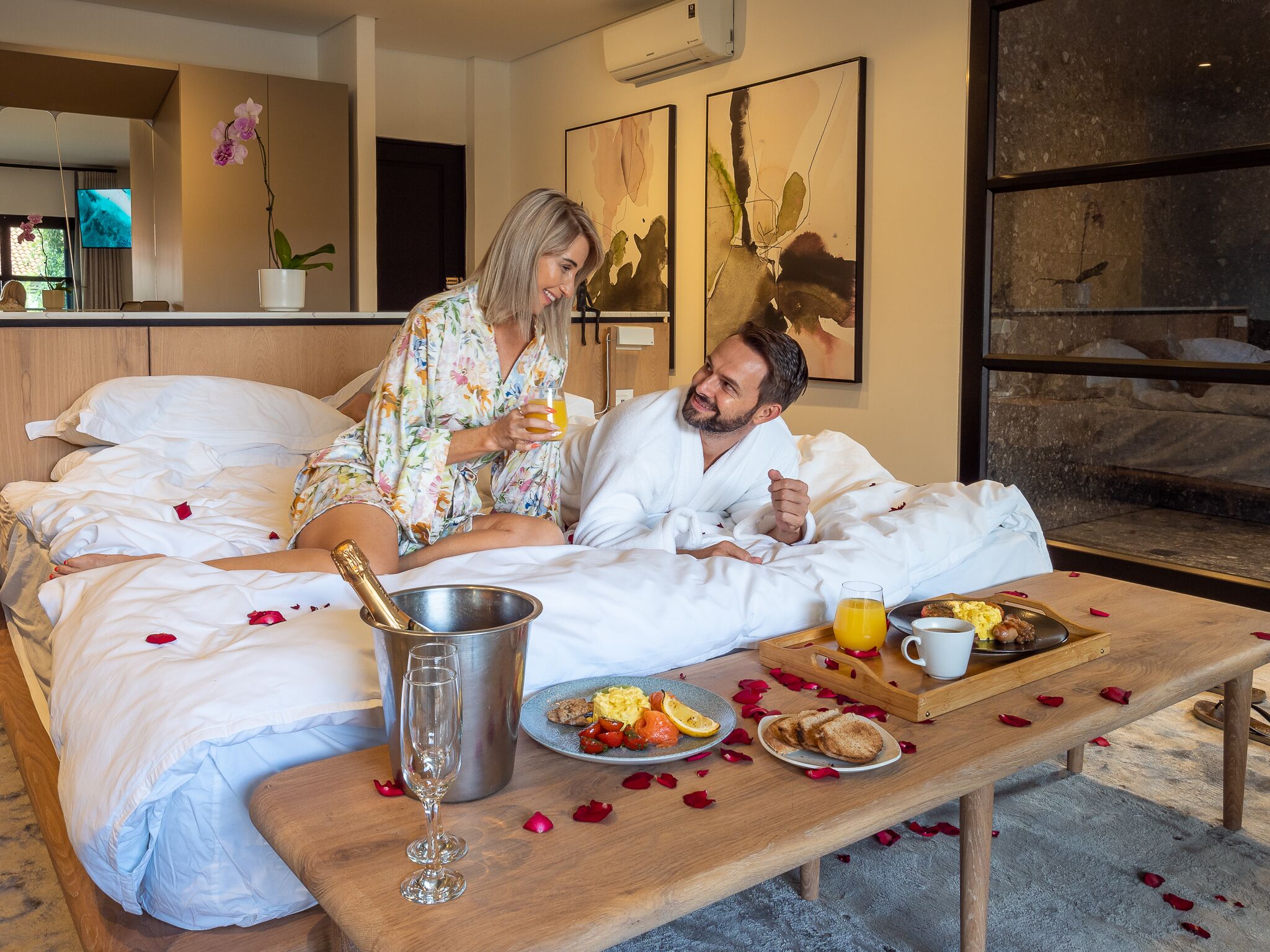 Een hotelkamer met een bed, een ontbijtplateau, een champagnefles en een glas sinaasappelsap.