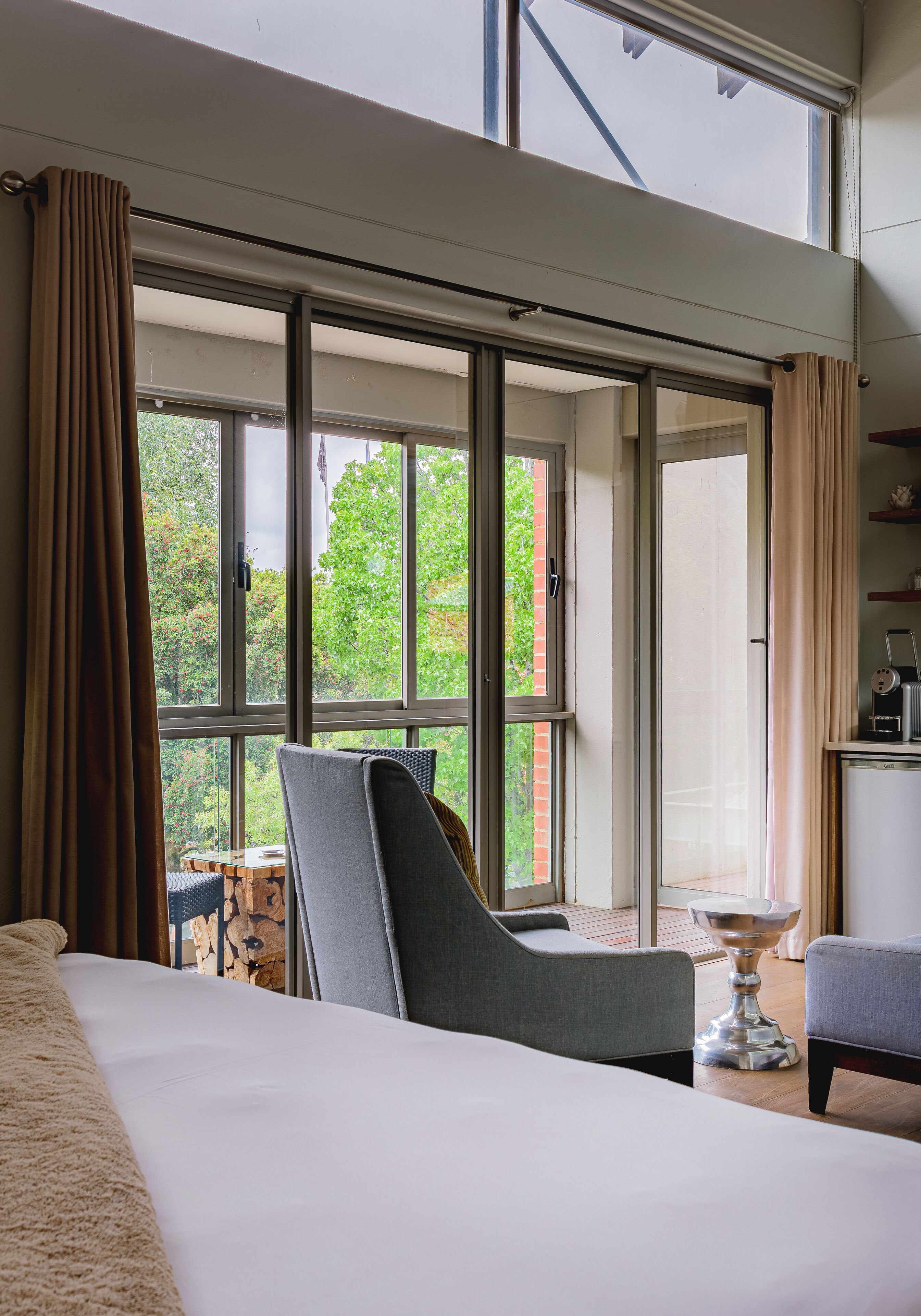 A hotel room with a large window, a bed, a chair, and a small table.
