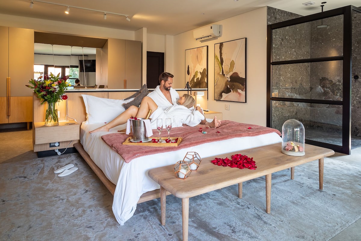 A modern bedroom with a bed, bedside tables, a wooden bench, and artwork on the walls.
