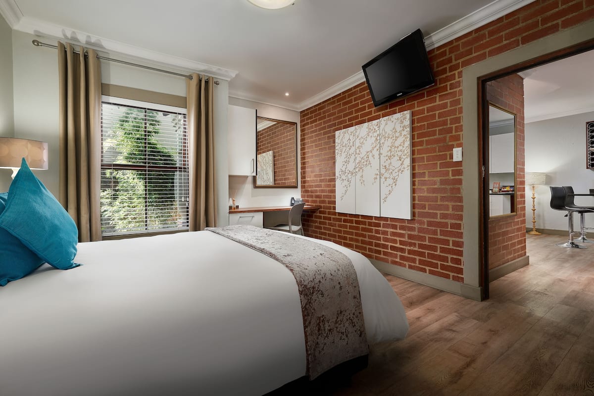 A hotel room with a large bed, a desk, a mirror, and a TV mounted on the brick wall.