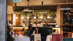An indoor dining area with tables and chairs, a bar area with shelves of bottles, and hanging plants. - Menlyn Boutique Hotel (Pretoria)