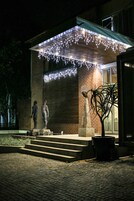 A building with a brick facade, a covered entrance area with string lights, and a statue of a person.