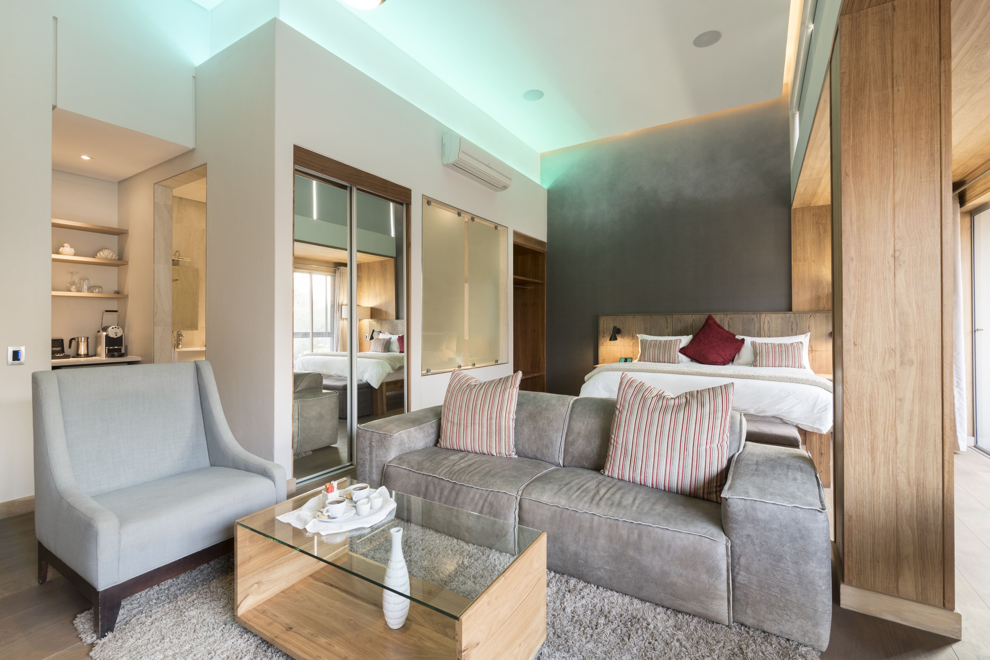 A modern living room with a sofa, a glass coffee table, and a bed with striped pillows.
