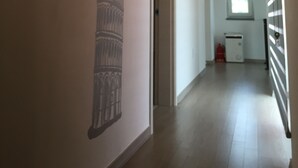 A hallway with a wall mural of the Leaning Tower of Pisa, a door, and a window with a radiator. - Incheon Airport Happy Place Guesthouse (Incheon)