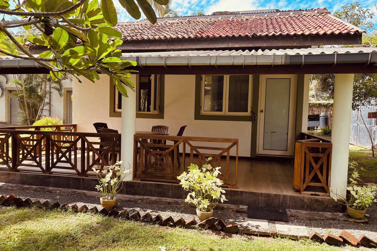 A house with a tiled roof, a porch with wooden furniture, and a small garden area.