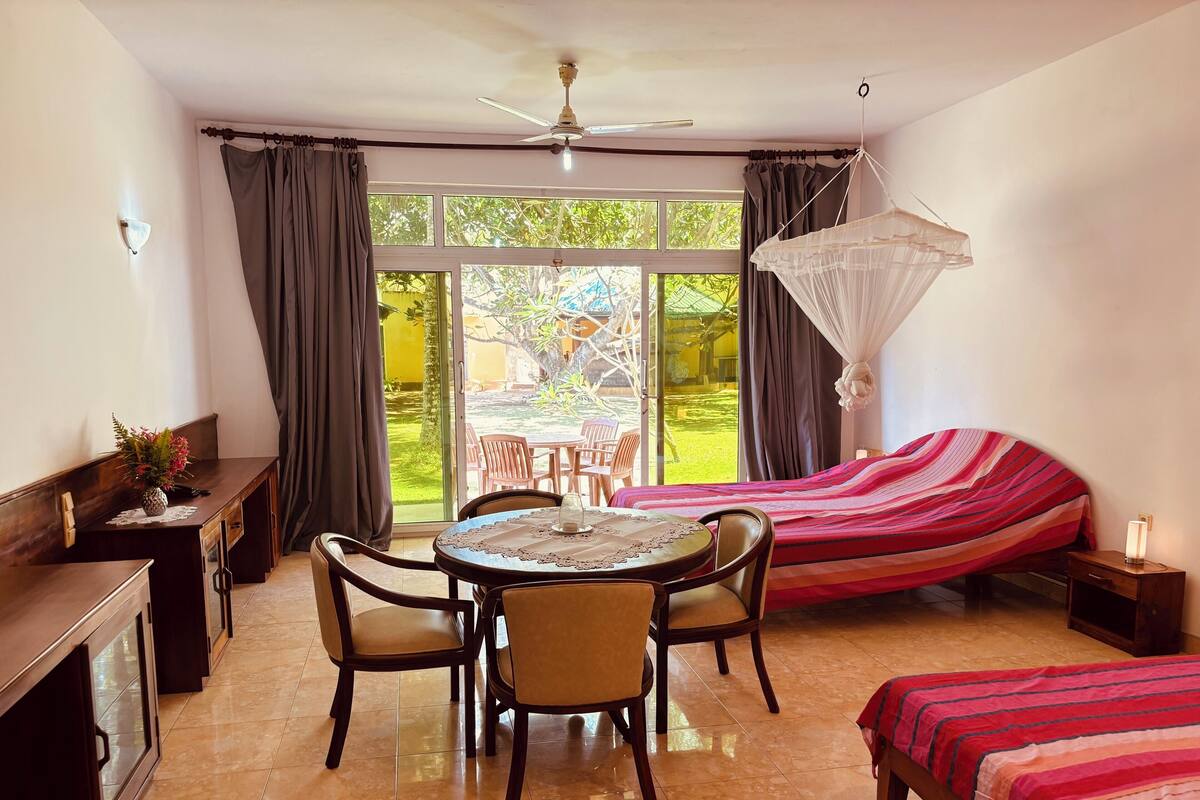 A room with a bed, a dining table with chairs, a small desk, and a window with curtains.