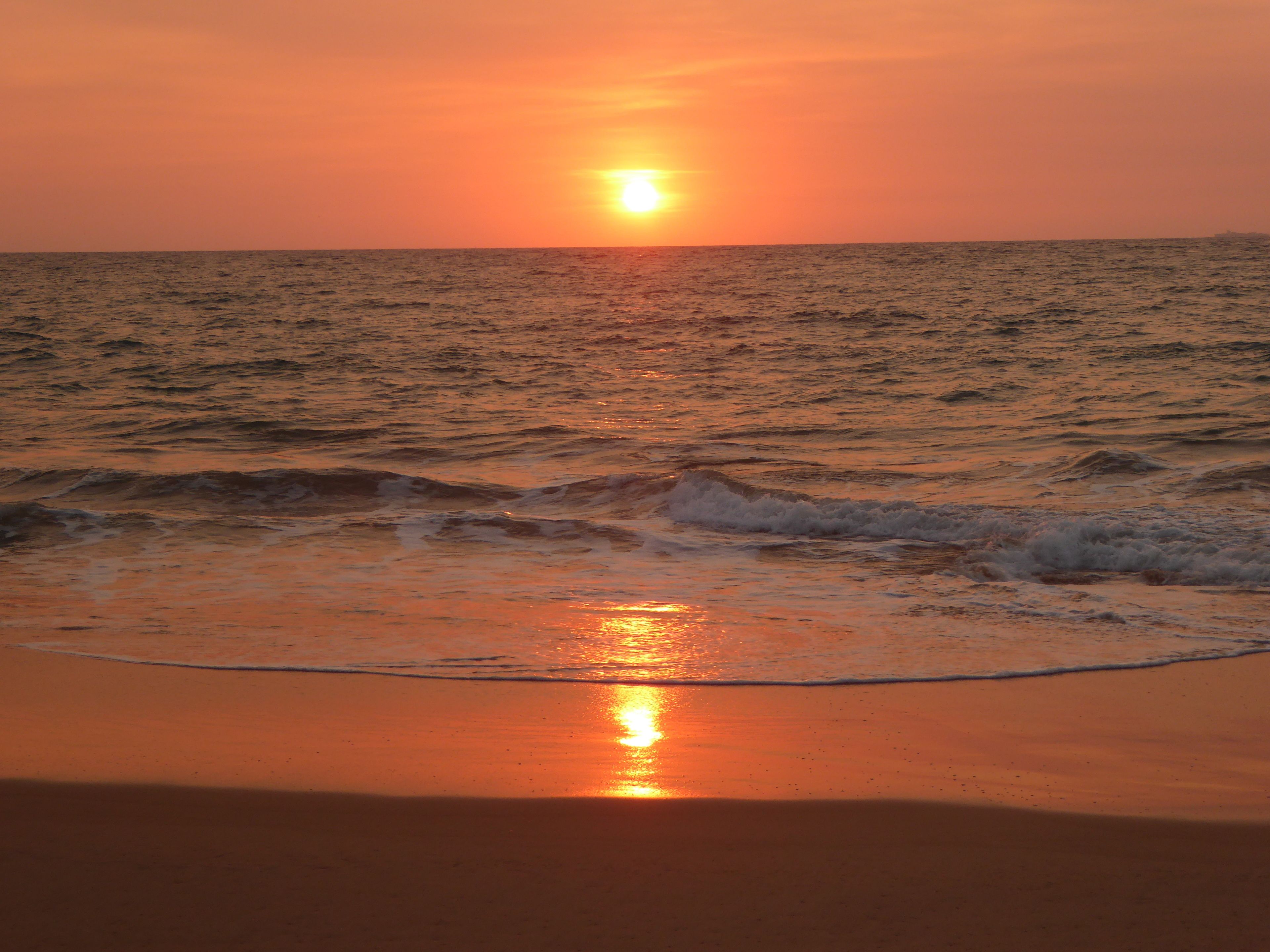 A sunset over the ocean with waves approaching the shore.