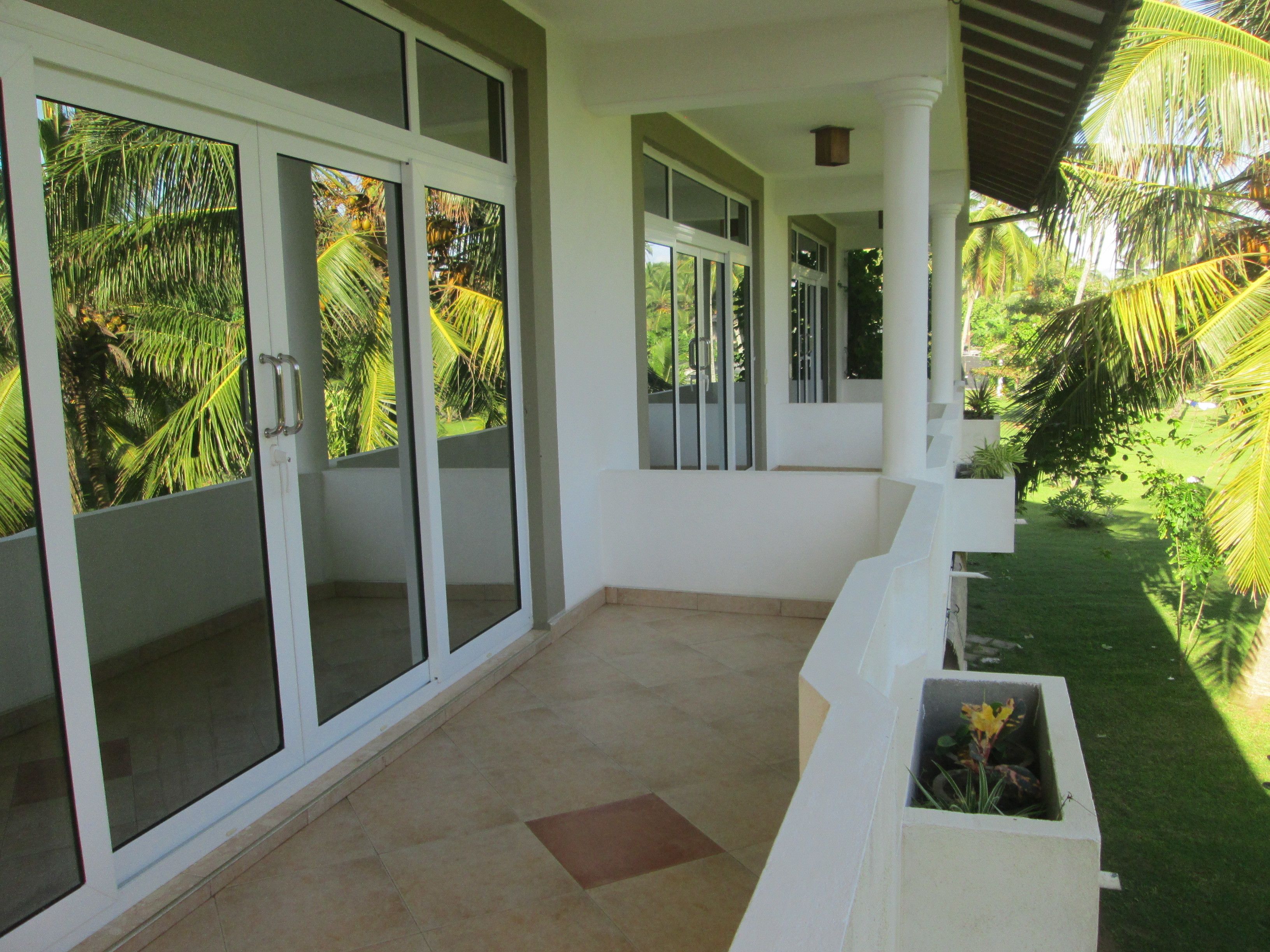 A covered outdoor area with a tiled floor, white walls, and large glass doors with palm tree views.