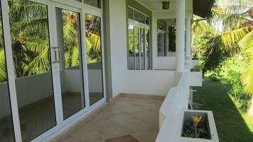 A covered outdoor area with a tiled floor, white walls, and large glass doors with palm tree views.
