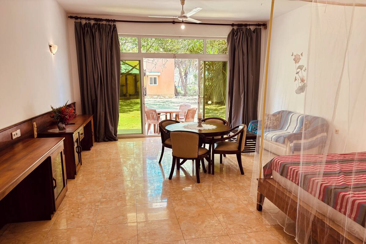 A room with a bed, a dining table with chairs, a small kitchen area, and a sliding glass door leading to an outdoor area.