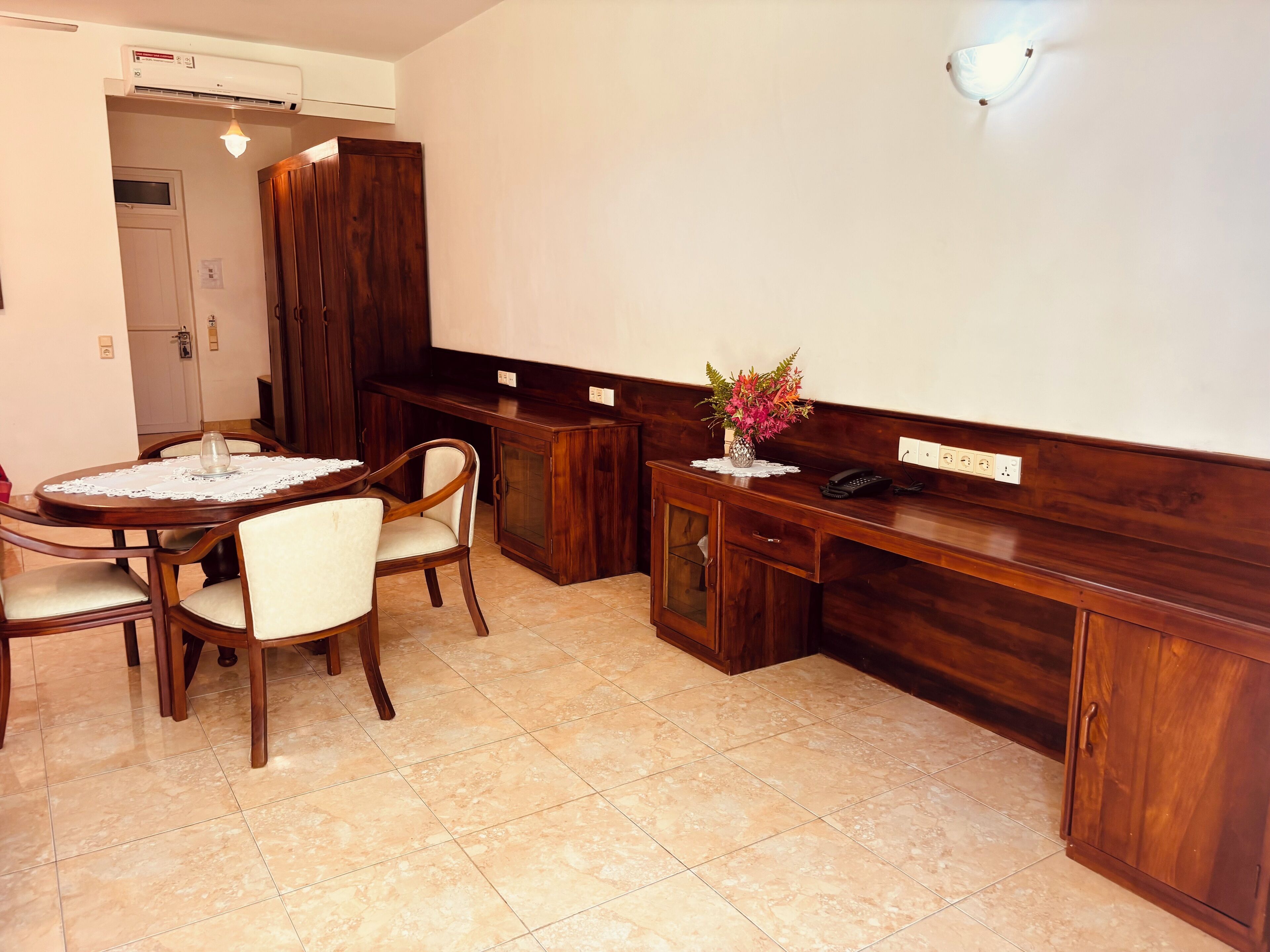 A dining area with a wooden table and chairs, a small cabinet with a telephone, and a vase with flowers on the counter.