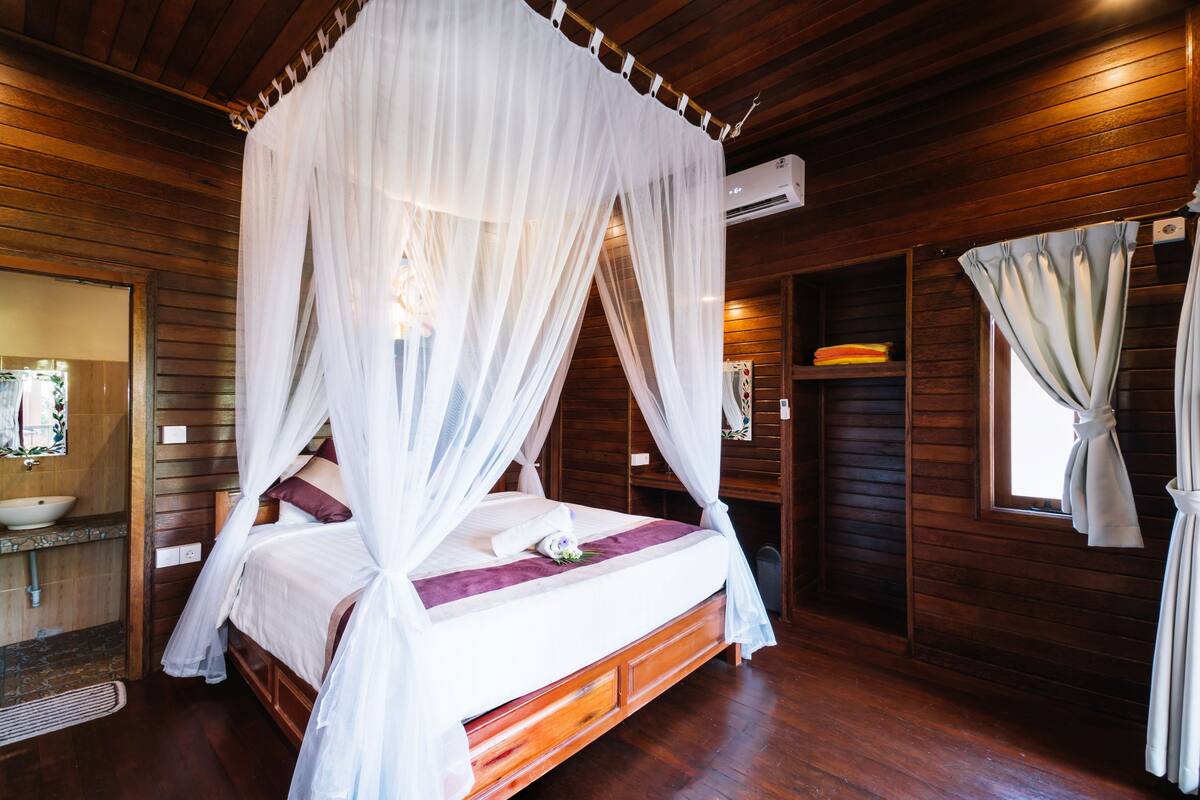 Une chambre à coucher de style cabane en bois, dotée d’un lit à baldaquin, d’un plancher en bois et d’une étagère intégrée agrémentée d’un miroir et d’objets décoratifs.