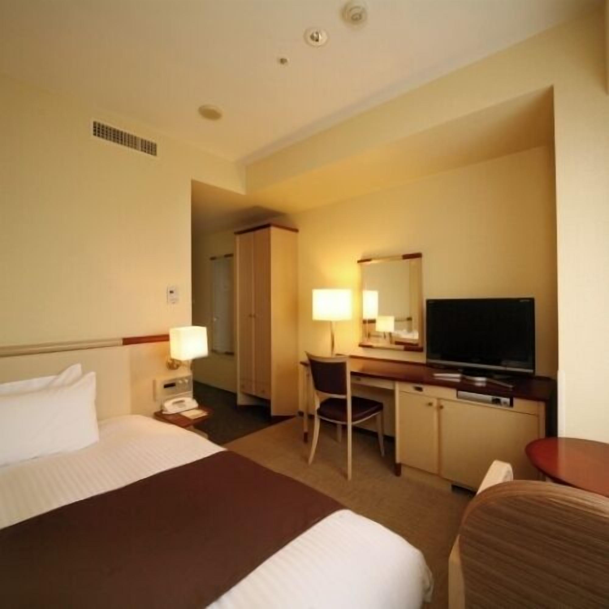 A hotel room with a bed, desk, chair, TV, and a wardrobe.
