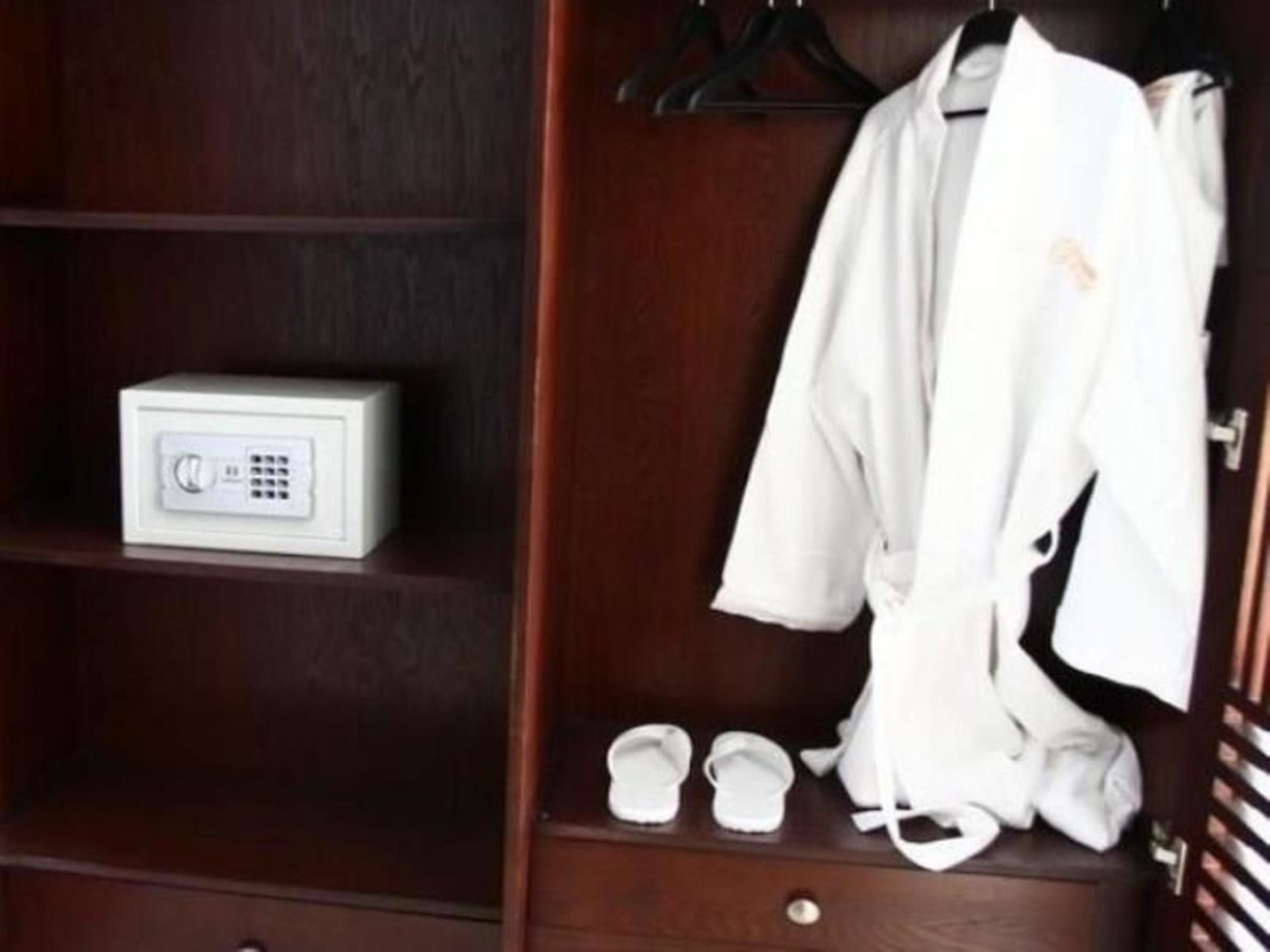 A wooden wardrobe with a white electronic device on the shelf, a white robe hanging, and a pair of white slippers on the lower shelf.