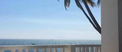 A balcony with a view of the ocean, a table, and two wicker chairs.