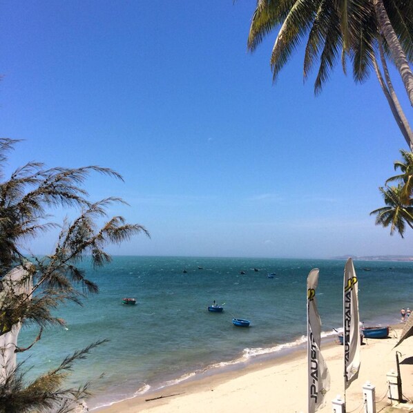 A beach with clear blue water, palm trees, and several boats. - Surf4You Residence (Mui Ne)