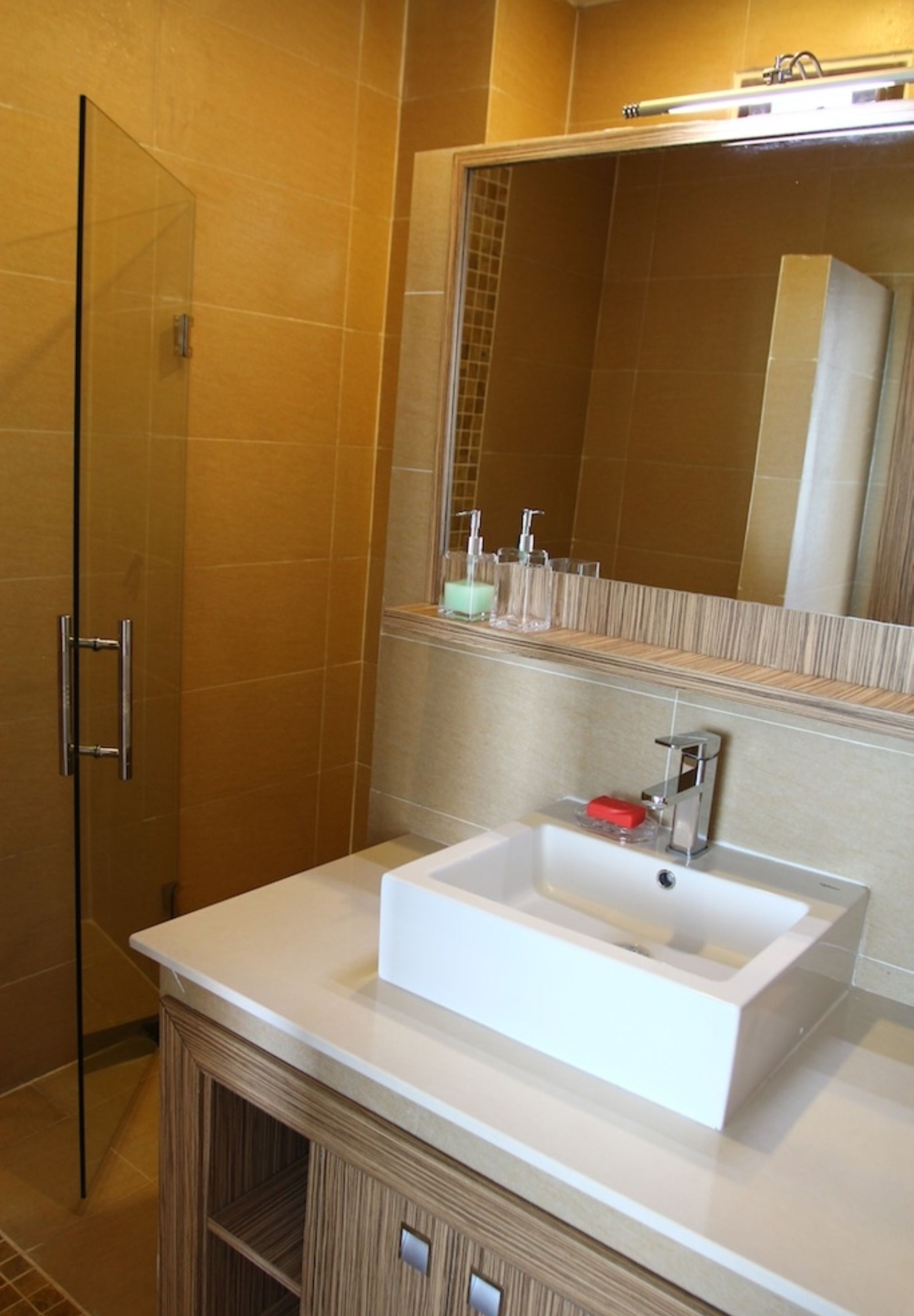 Une salle de bain avec une douche à parois de verre, un lavabo blanc avec un miroir au-dessus et un meuble en bois en dessous.