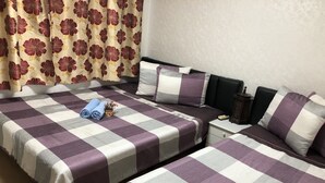 A hotel room with two beds, each with a purple and white checkered bedspread, a small bedside table with a lamp, and a curtain with a floral pattern. - Amuse Guest House - Hostel (Seoul)