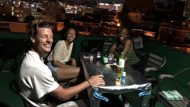 A rooftop terrace with a table set for three people, a cityscape view in the background, and a green railing. - Amuse Guest House - Hostel (Seoul)