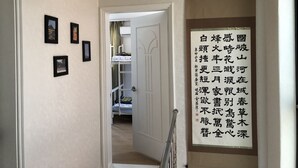 A hallway with framed pictures on the wall, a door leading to a room with bunk beds, and a vertical sign with Chinese characters. - Amuse Guest House - Hostel (Seoul)