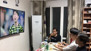 A room with a television displaying a sports event, a refrigerator, a dining table with food and drinks, and a bookshelf. - Amuse Guest House - Hostel (Seoul)