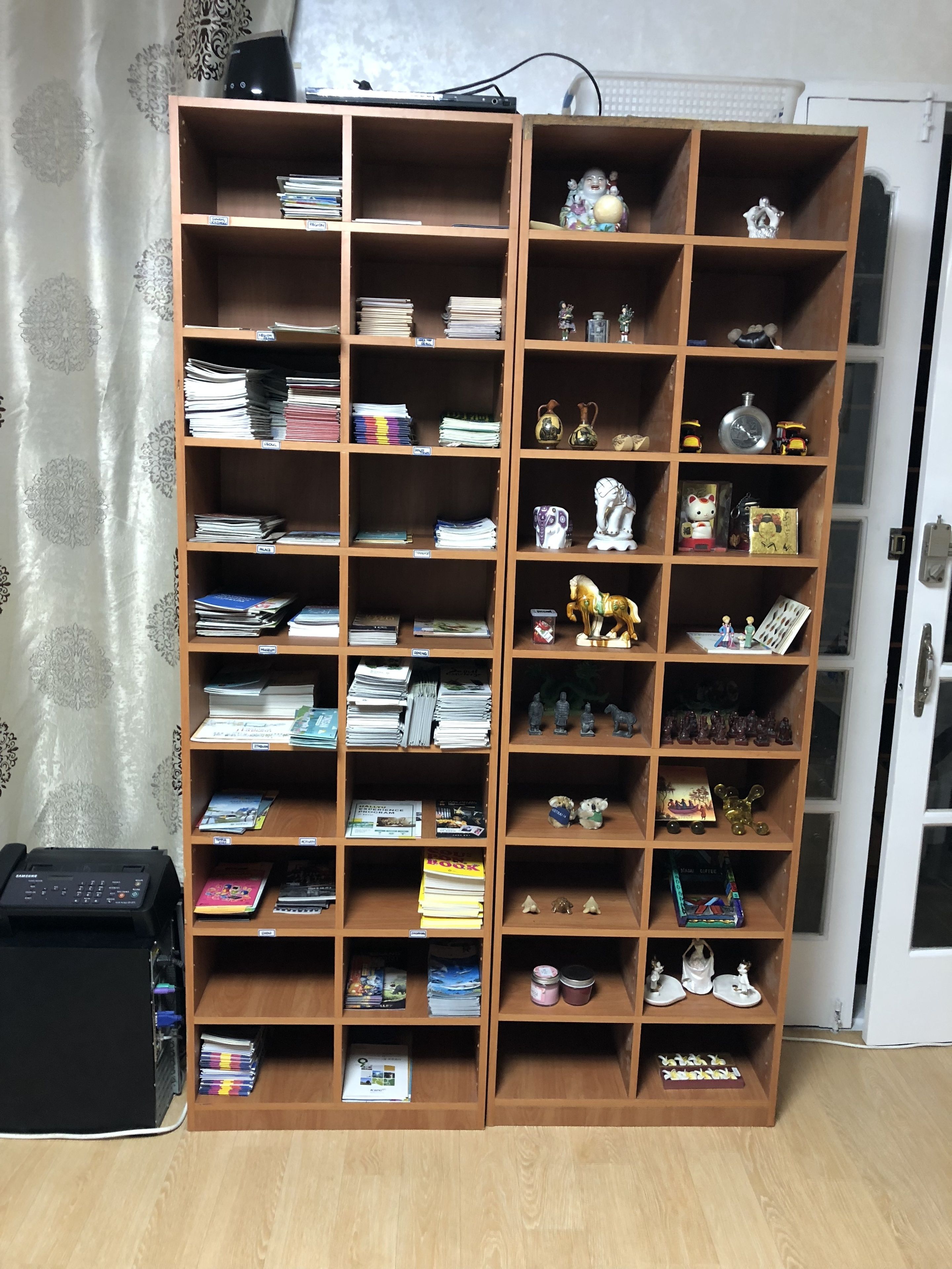 Une étagère en bois remplie de livres et d’objets décoratifs, placée à côté d’une imprimante noire et d’une porte.