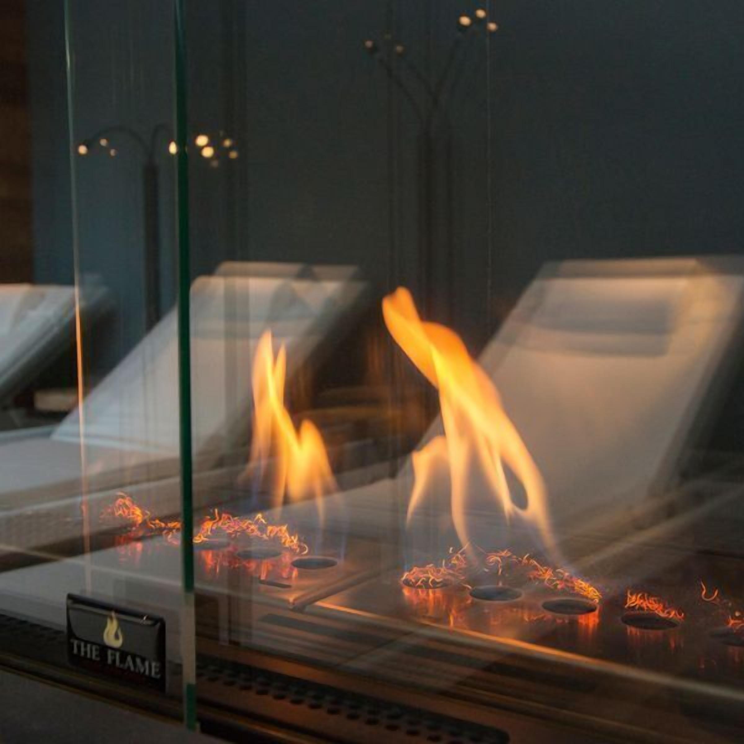 A glass enclosure with a fireplace, a sign reading "THE FLAME," and a reflection of a chair.