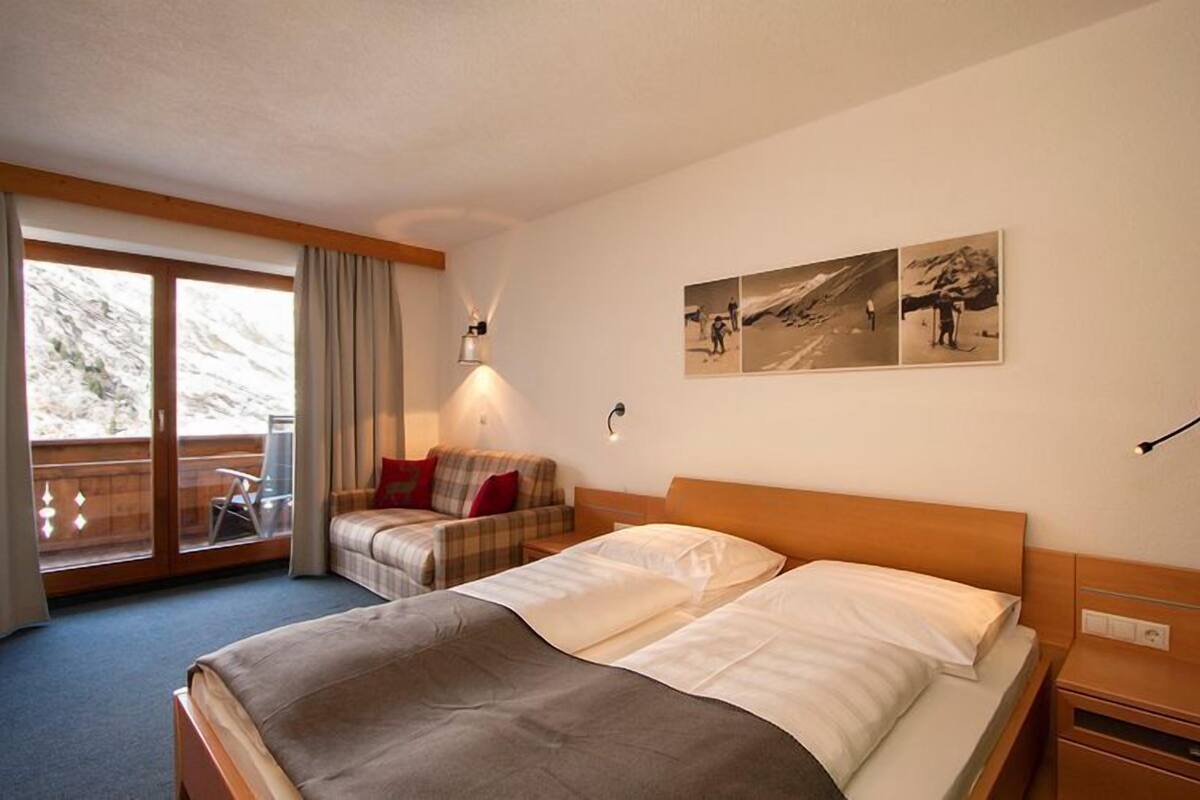 Een hotelkamer met een groot bed, een kleiner bed, een slaapbank en een balkon met uitzicht op de bergen.