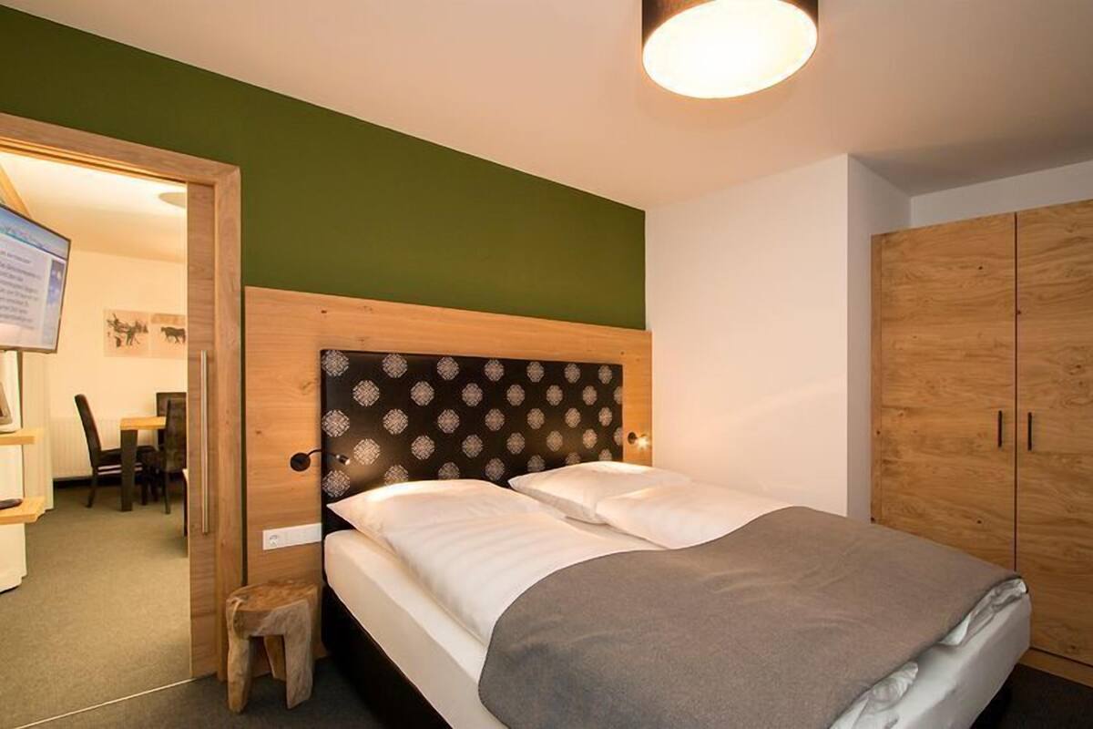 Een slaapkamer met een bed, een houten garderobe en een klein krukje.