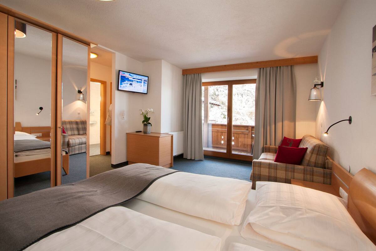 Een hotelkamer met een bed, een bank, een televisie en uitzicht op het groen.