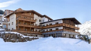 A multi-story hotel with wooden balconies and a stone facade, surrounded by snow-covered mountains. - Apartmenthaus Gurglhof (Soelden)