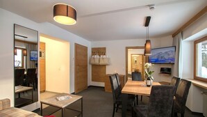 A modern hotel room with a dining area, a TV mounted on the wall, and a large window. - Apartmenthaus Gurglhof (Soelden)