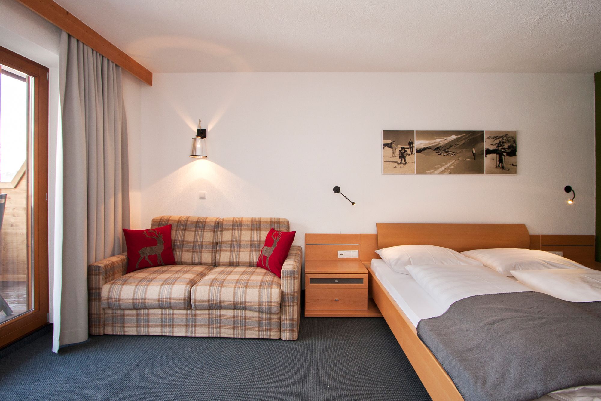 Una habitació d'hotel amb un llit, un sofà, una tauleta de nit i una làmpada penjada a la paret.